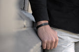 Well dressed man leaning against a wall wears a premium black leather bracelet from Rianrix Accessories 